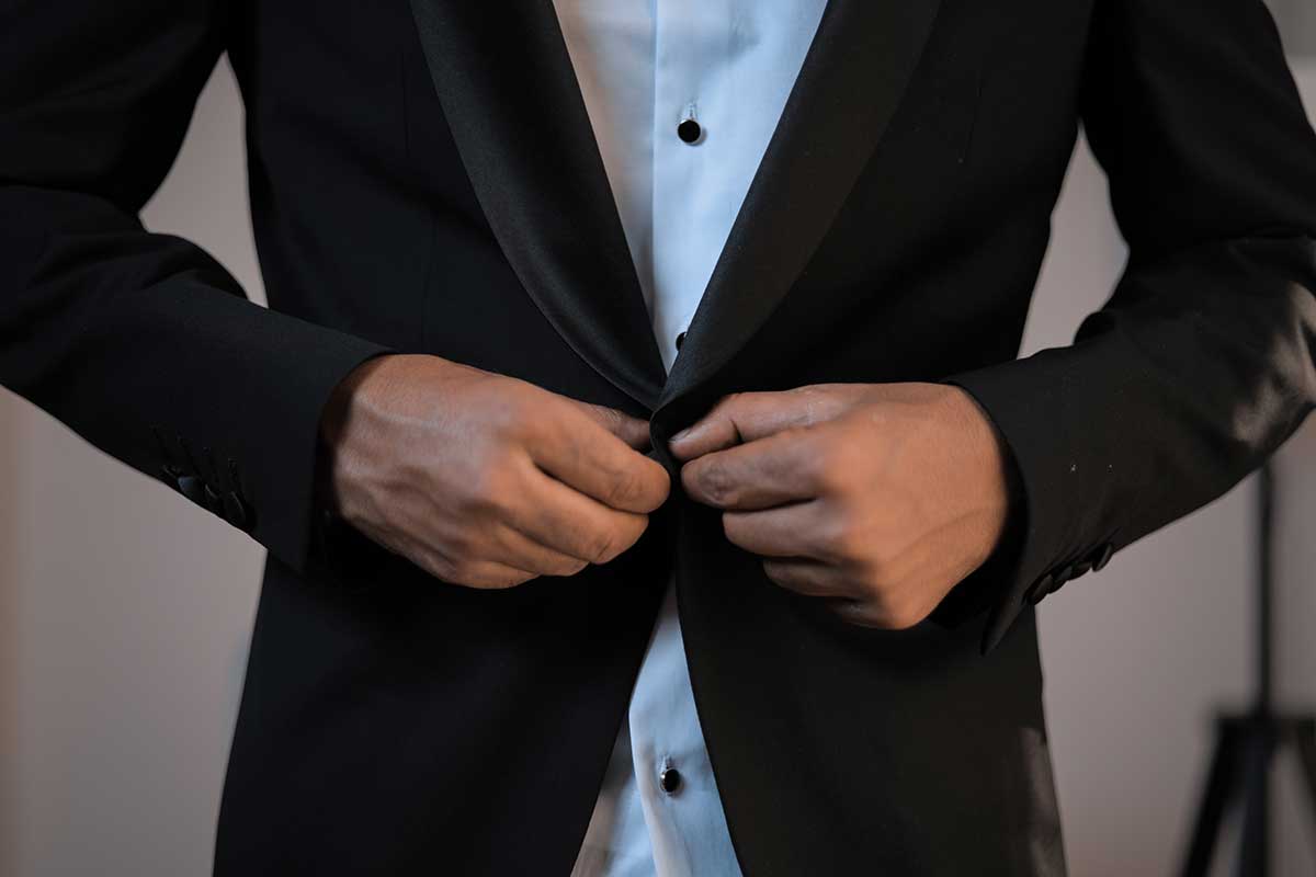 man buttoning top button of tuxedo jacket